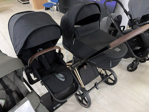 Black pushchair and carrycot set with twin canopies and wheels, front and side view
