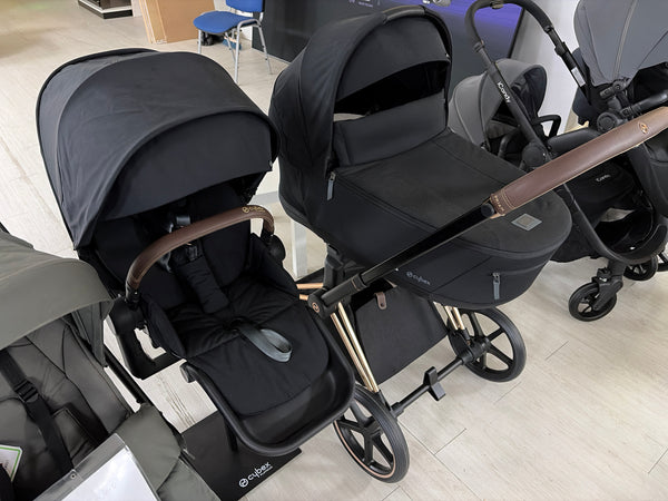 Black pushchair and carrycot set with twin canopies and wheels, front and side view