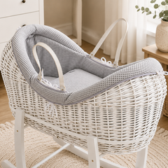 White wicker baby crib with gray cushion in a nursery setting