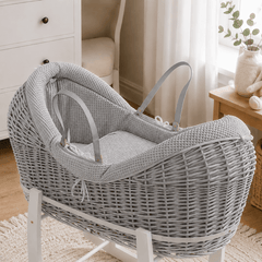 Grey wicker baby moses basket on white stand with padded cream waffle bedding