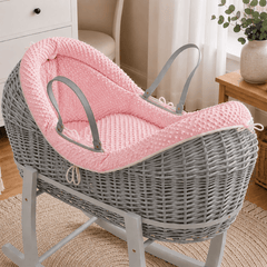 Grey wicker baby moses basket on white stand with padded pink waffle bedding