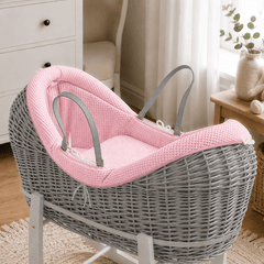 Grey wicker baby moses basket on white stand with padded pink waffle bedding