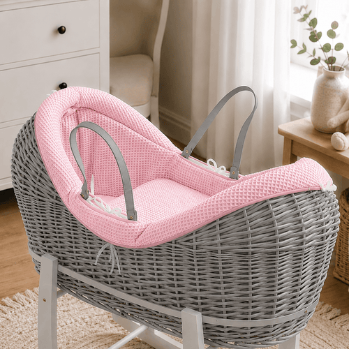 Grey wicker baby moses basket on white stand with padded pink waffle bedding