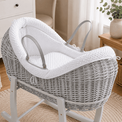 Grey wicker baby moses basket on white stand with padded light grey waffle bedding