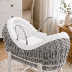 White wicker baby moses basket on white stand with padded white waffle bedding