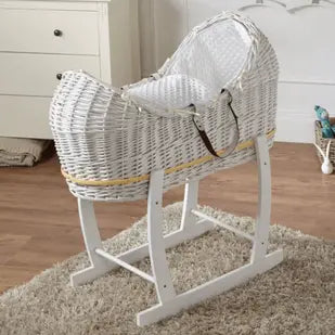White wicker baby crib with rocking stand on a wooden floor.
