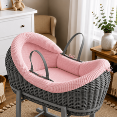 Gray wicker baby crib with pink cushion in a nursery setting