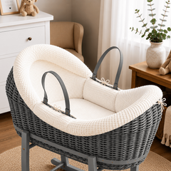 Gray wicker baby Moses basket with white cushion in a nursery setting