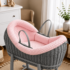 Gray wicker baby crib with pink cushion in a nursery setting