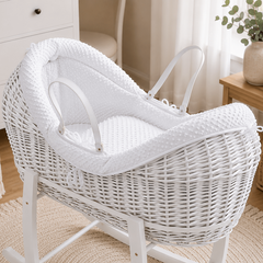 White wicker baby Moses basket with rocking stand in a nursery setting.