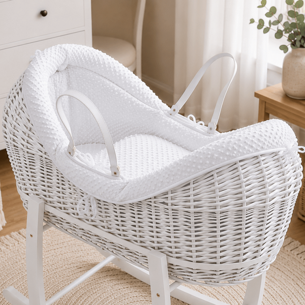 White wicker baby Moses basket with rocking stand in a nursery setting.