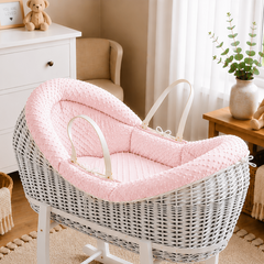 White wicker baby crib with pink cushion in a nursery setting