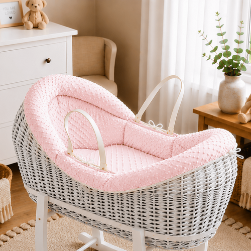 White wicker baby crib with pink cushion in a nursery setting